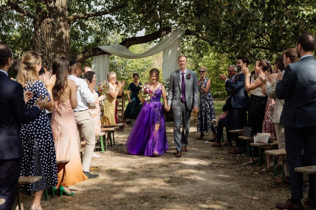 Mariés quittant leur cérémonie en extérieur sous les applaudissements des invités