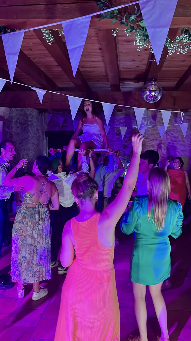 La mariée portée au-dessus de la piste par ses invités sous une boule à facettes en fin de soirée