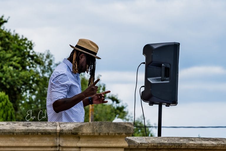 DJ Lexvolution au micro en extérieur, à côté d'une enceinte sur pied