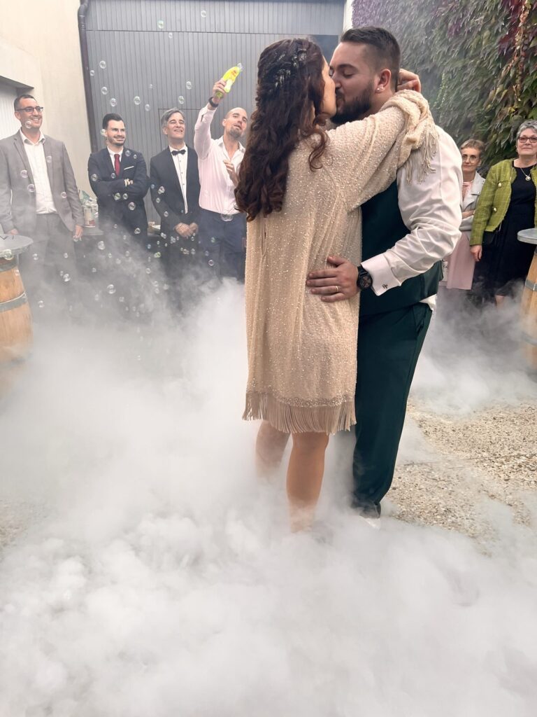 Les mariés s'embrassent pendant leur première danse en extérieur, dans la fumée lourde et les bulles de savon